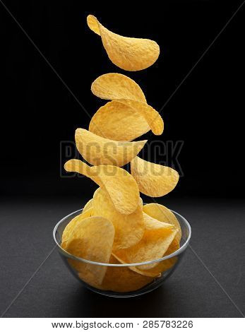 Potato Chips Falling Into Glass Bowl On Black Background