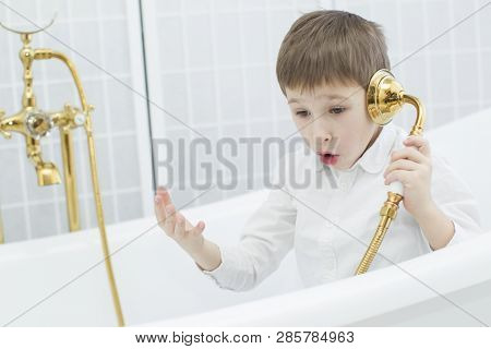 Baby In The Bathroom In Clothes.the Boy Sits In The Bath And Plays The Phone.talking On The Phone