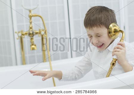 Baby In The Bathroom In Clothes.the Boy Sits In The Bath And Plays The Phone.talking On The Phone