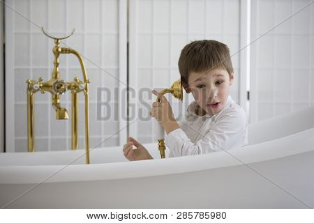 Baby In The Bathroom In Clothes.the Boy Sits In The Bath And Plays The Phone.talking On The Phone