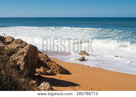 Rocks On The Clean Beach With Dark Yellow Sand. Foamy Waves Of The Atlantic Ocean. Horizon In The Ba