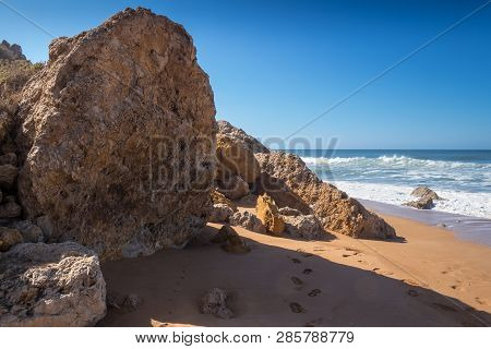 Rocks On The Clean Beach With Dark Yellow Sand. Foamy Waves Of The Atlantic Ocean. Horizon In The Ba
