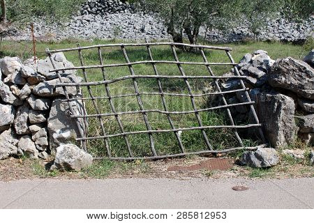 Tilted Improvised Backyard Wooden Doors Made From Wooden Sticks Supported With Makeshift Stone Wall 
