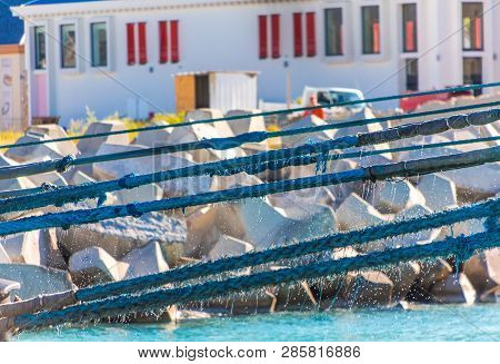 Blue Mooring Ropes Dripping Water Against Rock Seawall