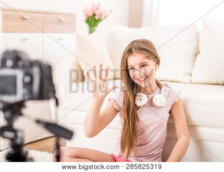 Young smiling videobloger teen girl is pointing at camera in living room