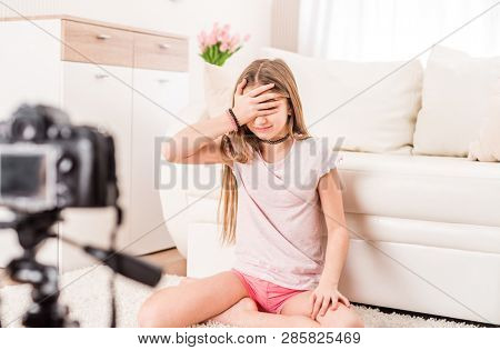 Smiling pretty teen girl recording video at home and hiding her face