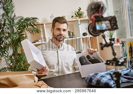 Fashion Blog. Smiling Male Blogger Opening Box With Sneakers While Recording New Video At Home On A 