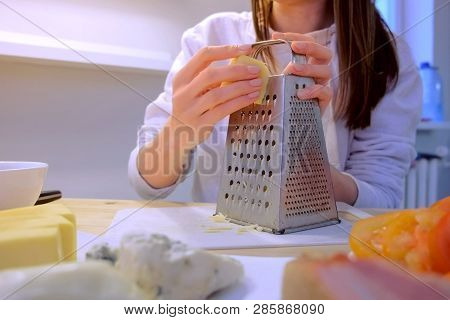 Woman Rubs Cheese On Grater At Home In The Kitchen. Hands Close-up.