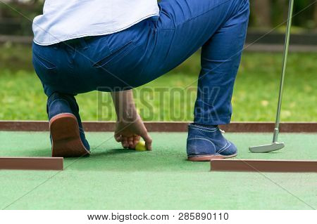 Minigolf Player Pulls A Yellow Ball Out Of The Hole, Rear View, Close-up