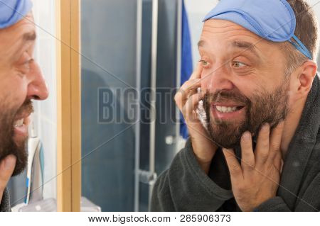Adult Man With Eyemask On His Forehead Feeling Fresh After Waking Up, Looking At Himself In Bathroom