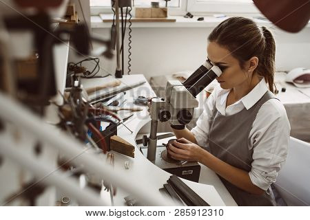 Focused On Work. Portrait Of Young Female Jeweler Looking At The New Jewelery Product Through Micros