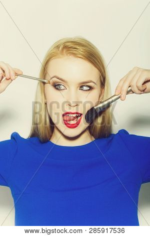 Girl Squinting Eyes On Silly Face With Makeup Brushes. Funny Woman Showing Tongue With Long Blond Ha