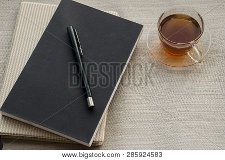 One Cup Of Tea Is On The Side Of The Pen, Placed On A Notebook To Work.