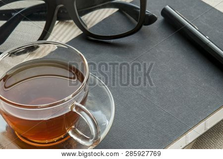 Tea, Glasses And Pens Placed On A Notebook For Work