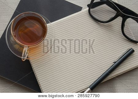 Tea, Glasses And Pens Placed On A Notebook For Work