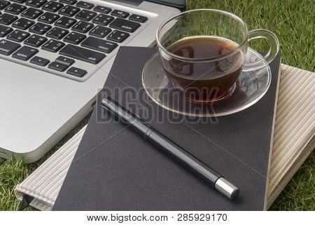 One Cup Of Tea And A Pen, Placed On Notebooks And Laptops In A Relaxed Lawn Area