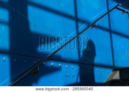 The Shadow Of A Man On A Bblue Surface With Handrail
