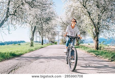 Happy Smiling Woman Rides A Bicycle On The Country Road Under Blossom Trees. Spring Is Comming Conce