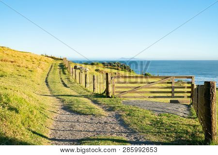 Track Along Fenceline Past Closed Farm Gate On Slpoing Hillside With View Out To Sea And Horizon.