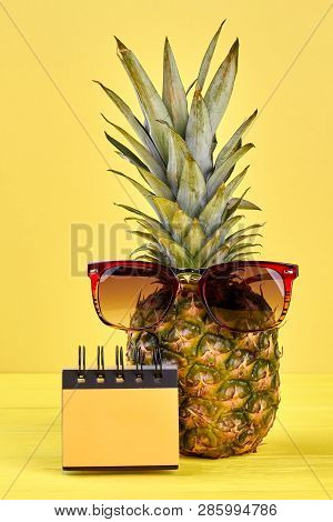 Pineapple With Sunglesses On Yellow Background. Fresh Pineapple Fruit With Blank Paper Notepad, Vert