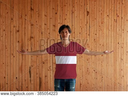 Man Wearing Latvia Flag Color Shirt And Standing With Arms Wide Open On The Wooden Wall Background, 