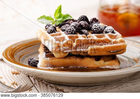 Belgian Waffles Served With Blackerries And Mint Leaf Dusted With Powdered Sugar On White Wooden Kit
