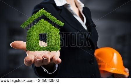 Real Estate Agent Holds In Palm Green Plant In Shape Of House. Woman In Business Suit With Safety He