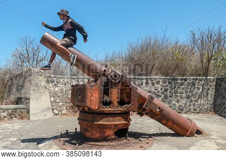 A Young Guy Sitting On Historic, Ancient Cannon. Mirjam Jepan On Lombok Island, Indonesia. Asian Tee