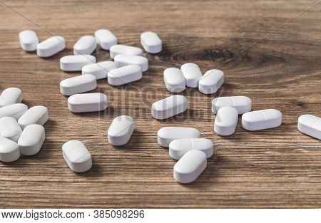 Medical Background. Several White Capsule Tablets Or Pills Scattered On Wooden Table. Healthcare Pha