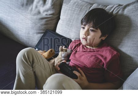 Portrait Of Kid Holding Video Game Or Game Console. Child Playing Game Online At Home, Young Boy Sit