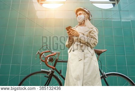 Woman in protective maskin, in helmet using her smartphone device. Female go to work on his sport retro bike. Girl standing on green background.