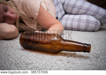 Woman Lying On The Floor With An Empty Alcohol Bottle Ans Sleeping, Overdosage And Female Alcoholism