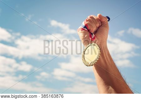 Gold medal winner held in hand raised against blue sky background