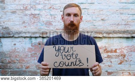 Man Shows Cardboard With Go Vote Sign On Brick Wall Urban Background. Voting Concept. Make The Polit