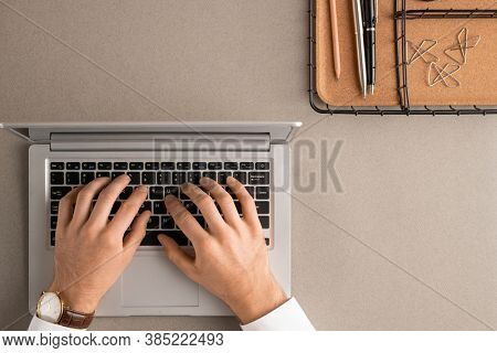 Top view of hands of contemporary elegant manager or office worker pressing buttons of laptop keypad while browing in the net by desk