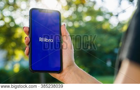 Berlin, Germany August 2019: Woman Hand Holding Iphone Xs With Logo Of Libra In The Park. Libra Face