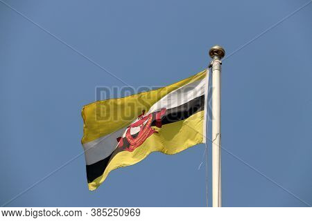 National Flag Of Brunei On Bright Blue Sky Background. Blown Away By Wind. Brunei Is One Of The Ten 