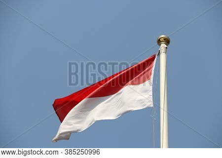 National Flag Of Indonesia On Bright Blue Sky Background. Blown Away By Wind. Indonesia Is One Of Th