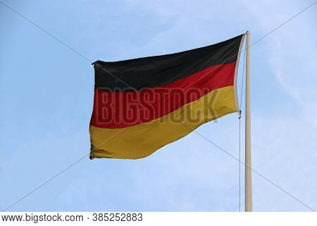 Tri Color Of German Flag, Black Red And Yellow Color On Blue Sky Background. Blown Away By Wind.