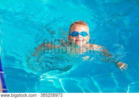 Cute Happy Little Boy In Goggles Swimming In The Swimming Pool