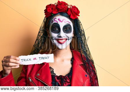 Woman wearing day of the dead costume holding trick or treat paper looking positive and happy standing and smiling with a confident smile showing teeth 