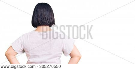 Brunette woman with down syndrome wearing casual white tshirt standing backwards looking away with arms on body 