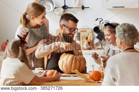 Happy Multi Generational Family Smiling And Carving Jack O Lantern From Pumpkin While Gathering Arou