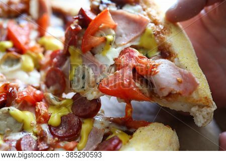 Close-up Of Persons Hand Taking Delicious Slice Of Baked Pizza. Bacon Sausages Double Cheese And Tom