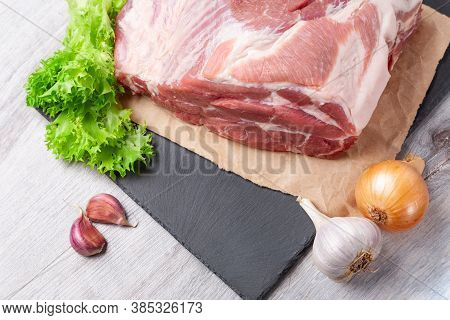 A Piece Of Uncooked Meat Of Pork Neck On Black Stome Plate With Ingredient On Gray Table. Ready To B