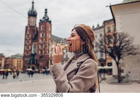 Woman Eating Bagel Obwarzanek Traditional Polish Cuisine Snack On Market Square In Krakow. Travel Eu