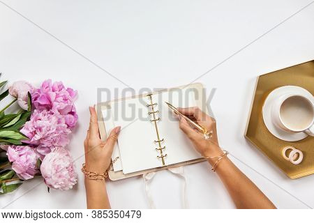 Well-groomed Woman Hands Is Writing In Diary With Stationery Supplies Set Onside And Peonies Bouquet