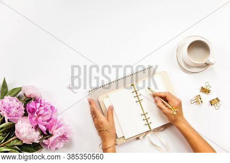 Well-groomed Woman Hands Is Writing In Diary With Stationery Supplies Set Onside And Peonies Bouquet