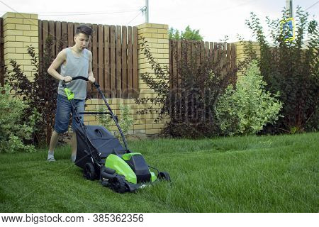 A Teenager Mows The Lawn With A Lawn Mower.