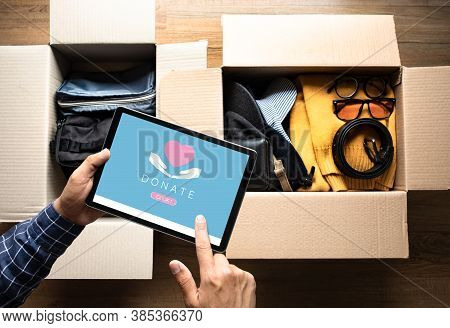 Donation Concepts With Young Person Packing Accessories Clothing And Using Digital Tablet For Donate